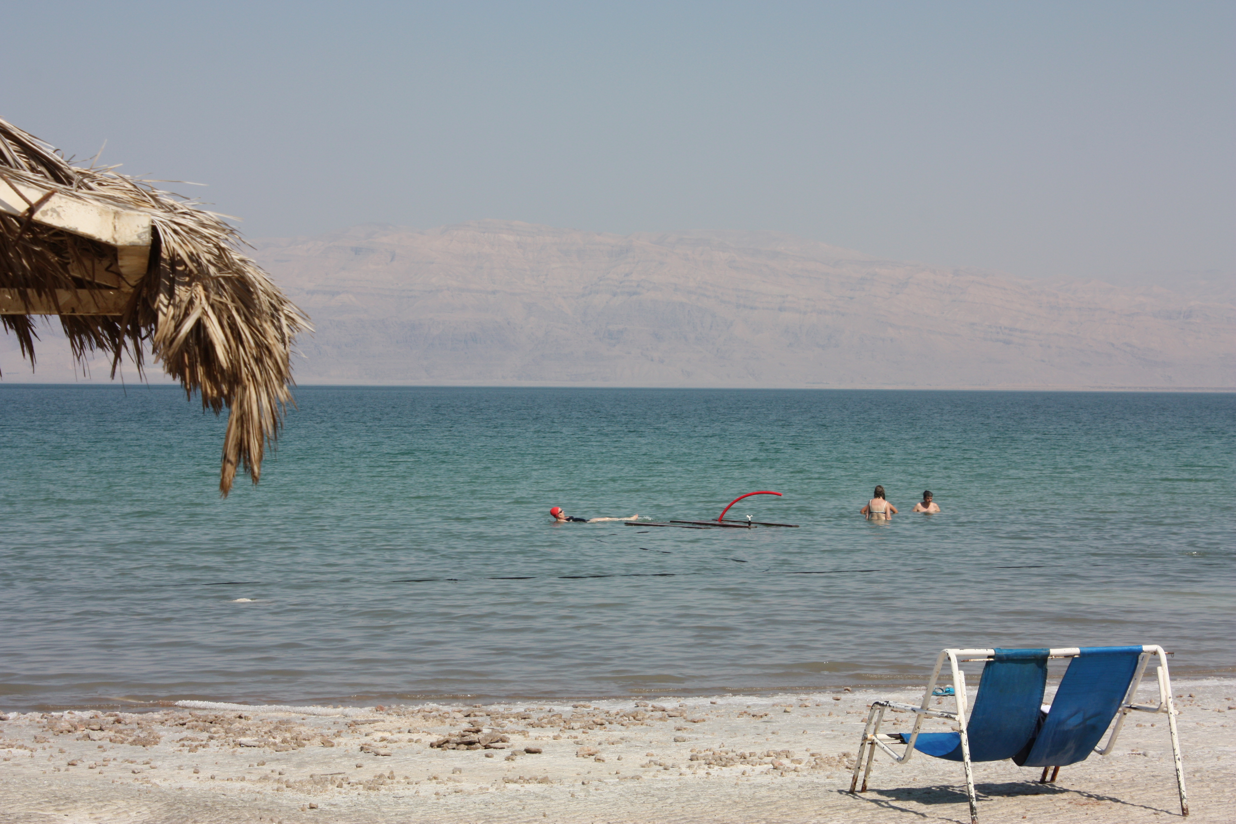 Strand des Toten Meeres mit Sonnenschirm, zwei Liegestühlen und Badegästen